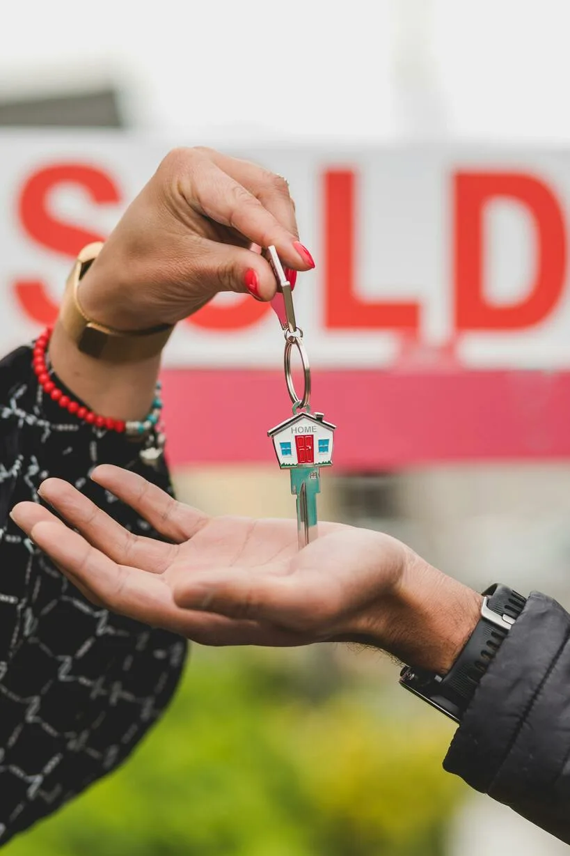 Hands exchanging house keys in front of a sold sign