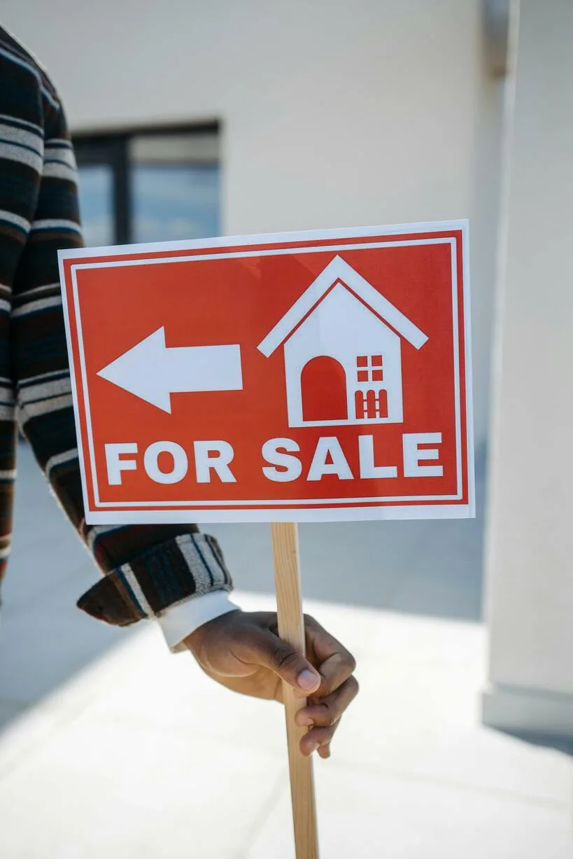 A hand holding a for-sale real estate sign outdoors